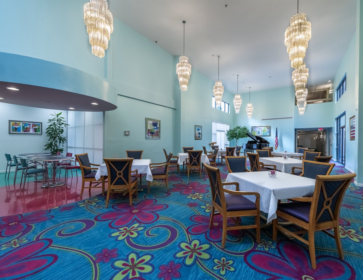 A vibrant restaurant interior with colorful carpeting, elegant chandeliers, and neatly arranged tables and chairs.