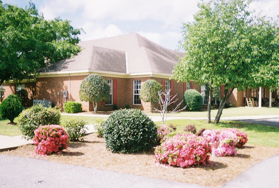 A well-maintained brick house surrounded by a landscaped garden with various shrubs, bushes, and trees.