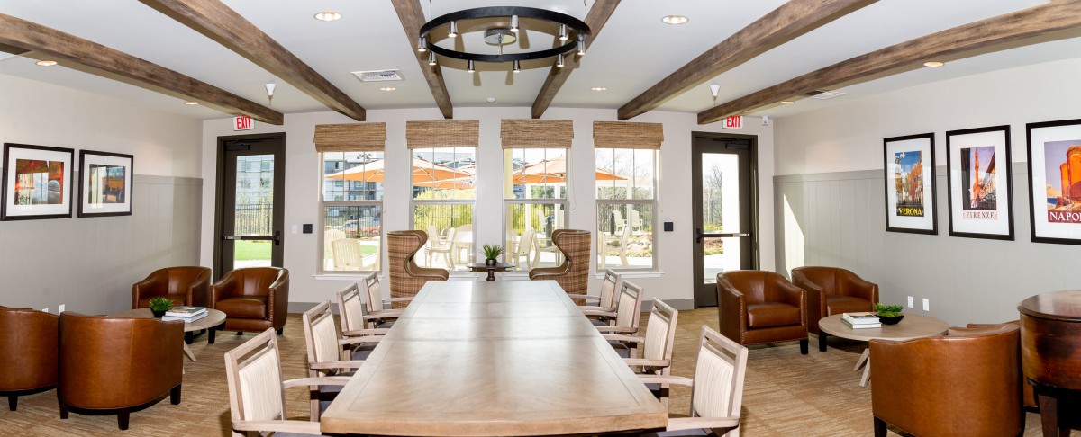 A modern conference room with a large meeting table and chairs, featuring ample natural light through several windows.