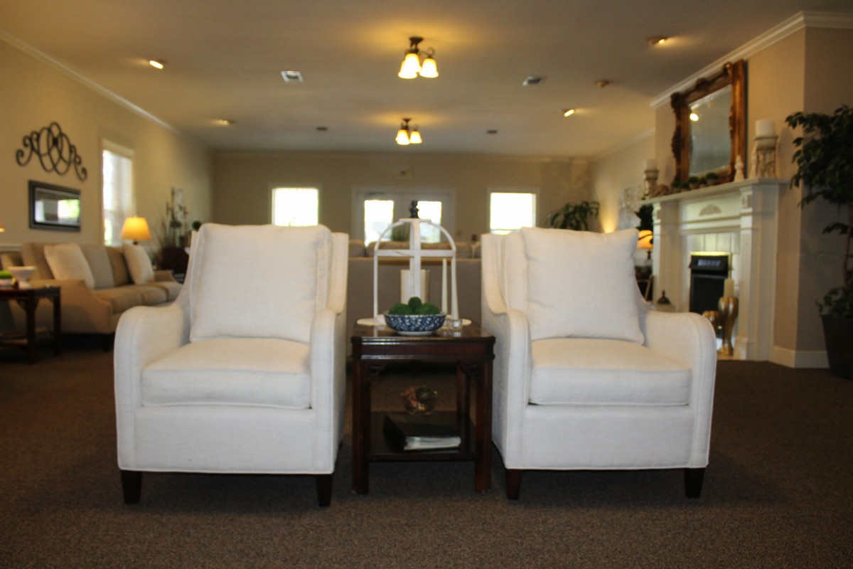 A cozy living room with two white chairs and a small wooden table under warm lighting.