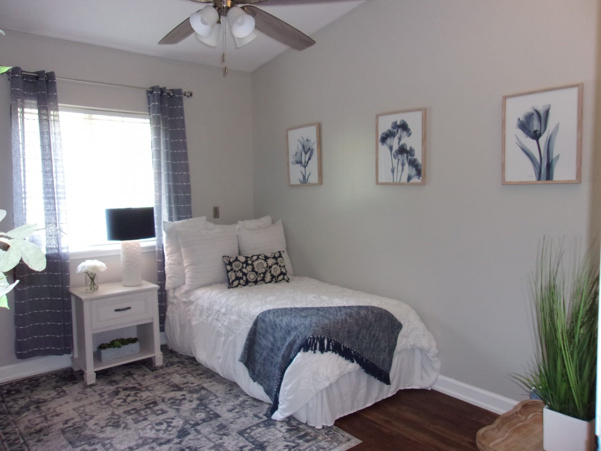 A cozy and well-decorated bedroom with a single bed, featuring neutral tones, artistic wall decor, a rug, and a bedside table.