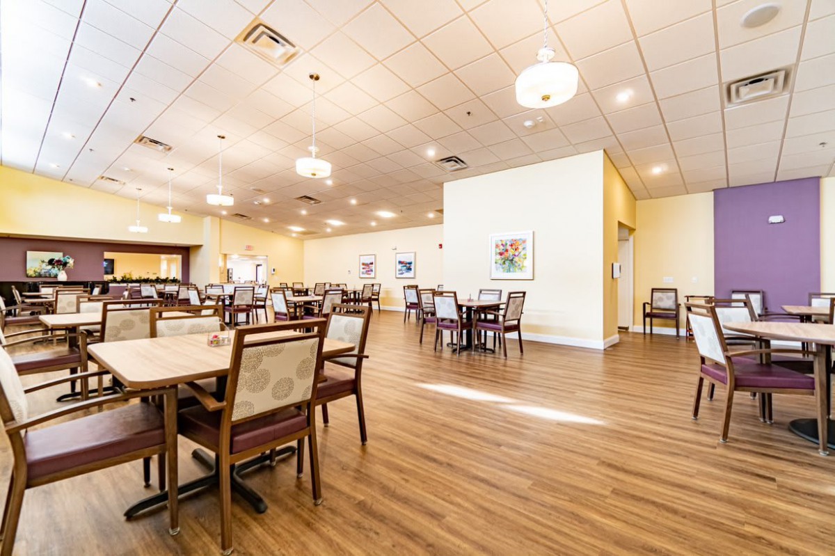 Spacious dining area with neatly arranged tables and chairs, featuring ceiling lights and a wooden floor.
