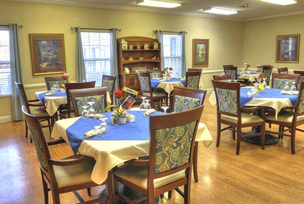 A neatly arranged dining room with tables set for a formal meal, featuring blue and beige tablecloths and decorative elements.