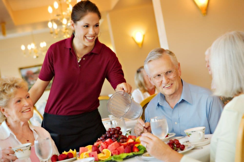 A server pouring water for an elderly man at a restaurant.