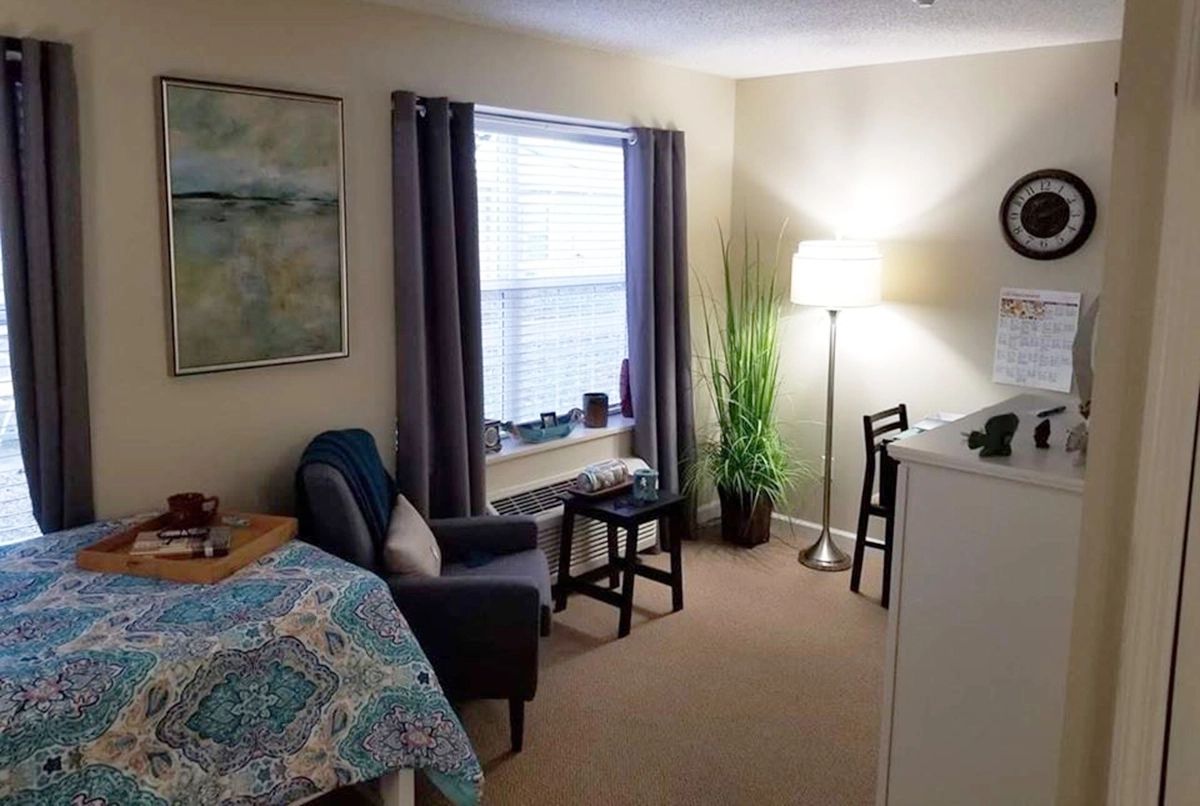A cozy bedroom with a bed, chair, lamp, and indoor plant by the window.