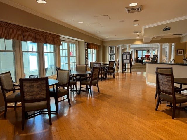 A spacious dining area with wooden floors and large windows, featuring tables and chairs.