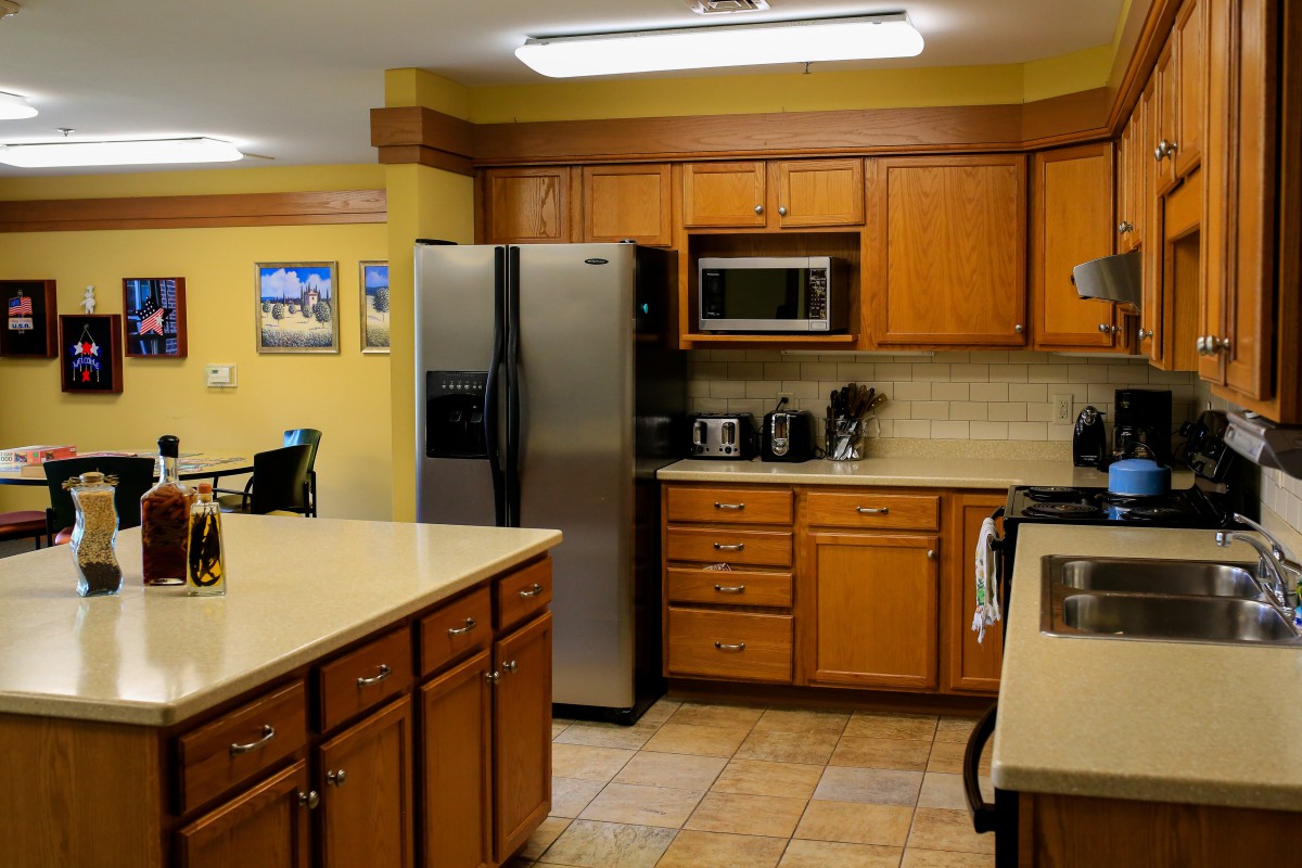 A modern kitchen with wooden cabinets, stainless steel appliances, and a tiled floor.