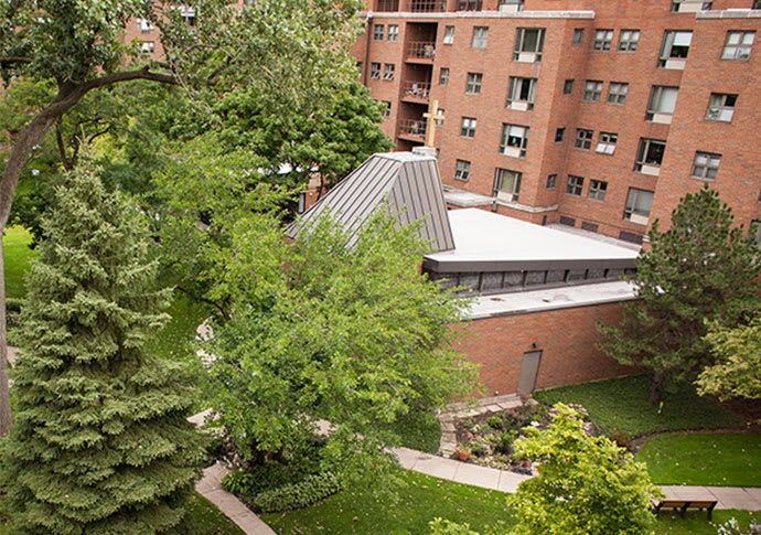 A view of a brick building surrounded by lush greenery and trees in an urban setting.