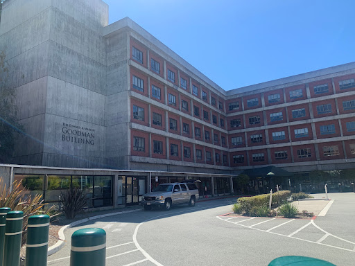 A modern multi-story building with a parking area, captured in bright daylight.