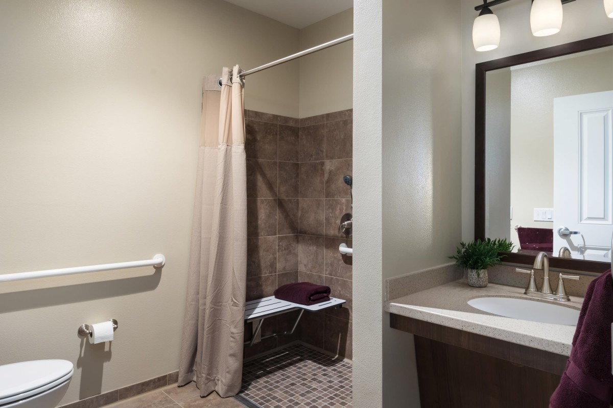 An accessible bathroom with a tiled shower area, curtain, and sink.