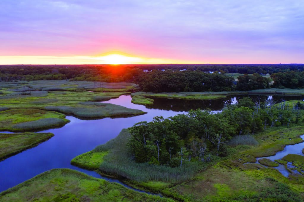 A picturesque view of a river winding through lush wetlands at sunset.