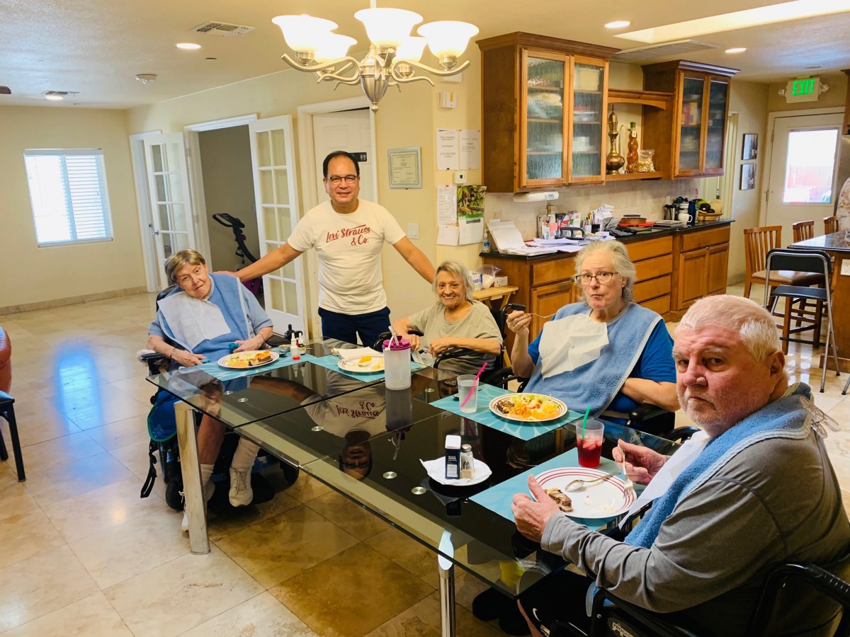A group of people gathered around a table enjoying a meal together in a kitchen setting.