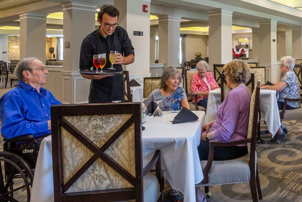 A waiter serves drinks to a group of customers seated at a restaurant table.
