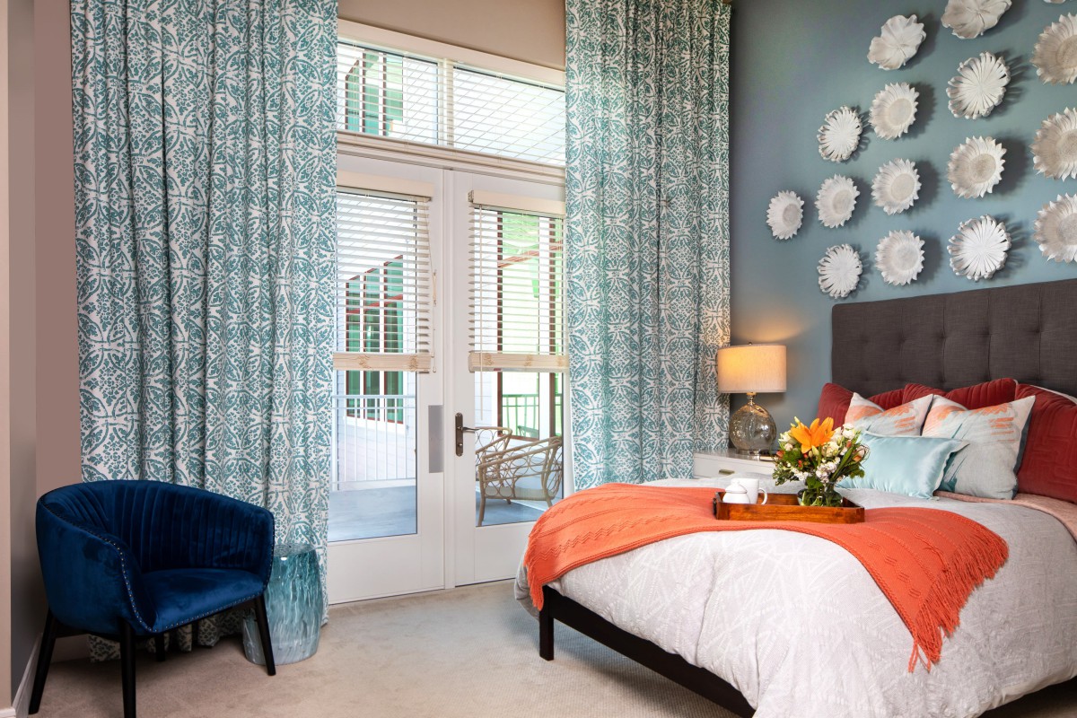 A stylish bedroom interior with a colorful bed, decorative curtains, and modern wall art.