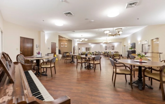 A spacious dining area with empty tables and chairs, featuring a piano and elegant chandeliers.