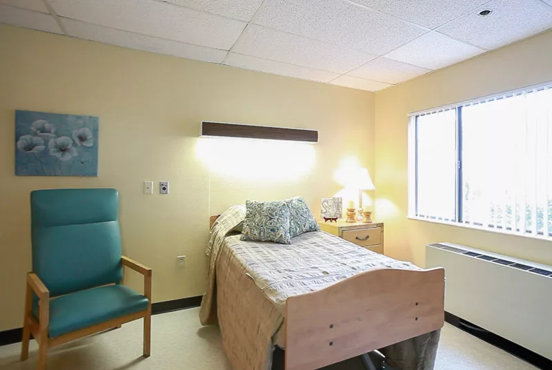 A clean and minimalist hospital room with a single bed and basic furnishings.