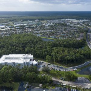Aerial view of a suburban area with roads, buildings, and surrounding forested landscape.