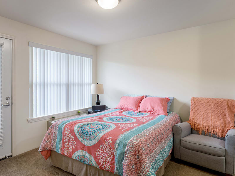 A cozy bedroom featuring a colorful bedspread, a cushy couch, and ample natural light through large windows.