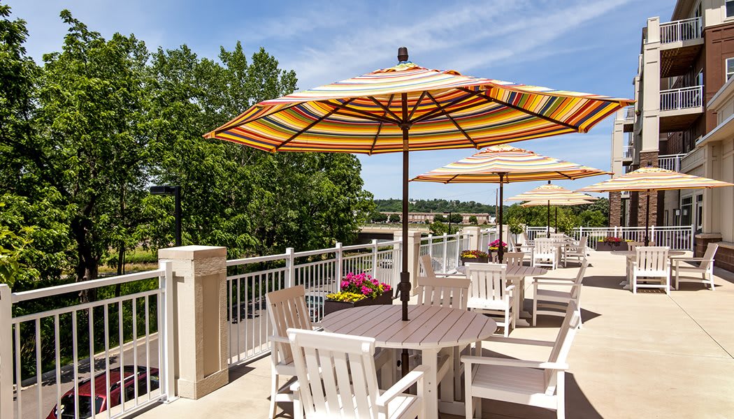 A sunny outdoor patio with tables and striped umbrellas, surrounded by lush greenery.