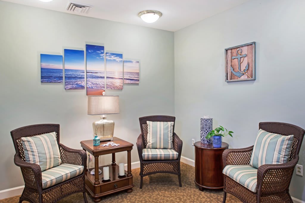 A cozy waiting room with comfortable chairs, a lamp, and decorative artwork on the walls.
