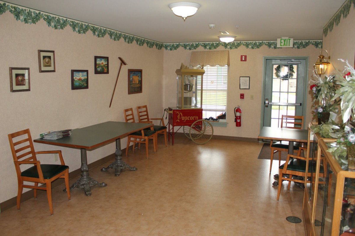 An empty dining area with tables and chairs, decorated with wall ornaments and a fire extinguisher near the entrance.