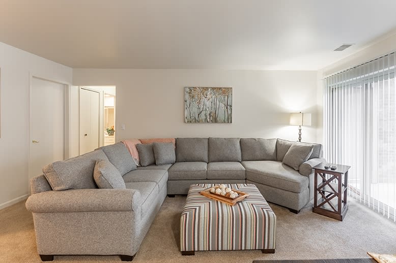 A cozy living room with a gray sectional sofa and striped ottoman, complemented by soft lighting and wall art.