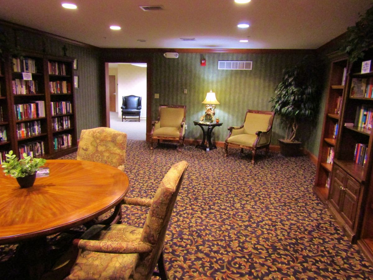 A cozy living room with upholstered chairs, a round table, and a bookshelf under warm lighting.