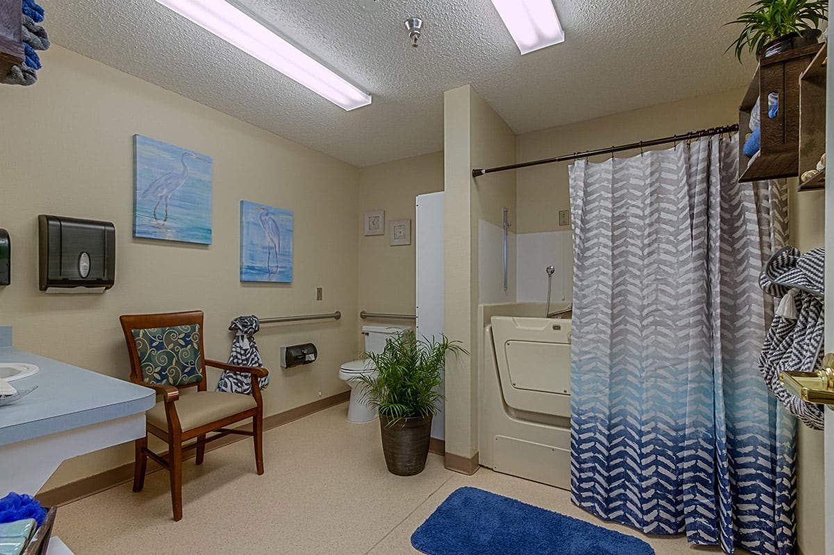 A well-lit, accessible bathroom with a walk-in bathtub, chair, and blue-themed decor.