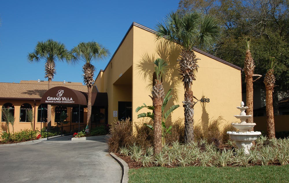 A restaurant with a yellow exterior and palm trees in front, featuring an awning over the entrance.