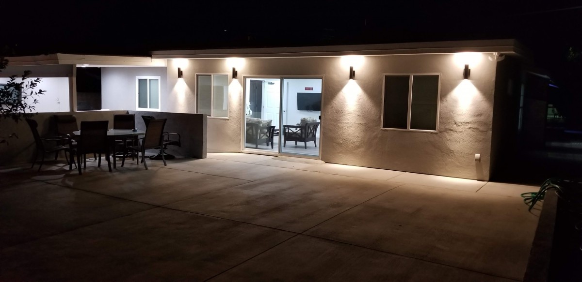 A well-lit patio area at night featuring a house exterior with glass doors and windows.