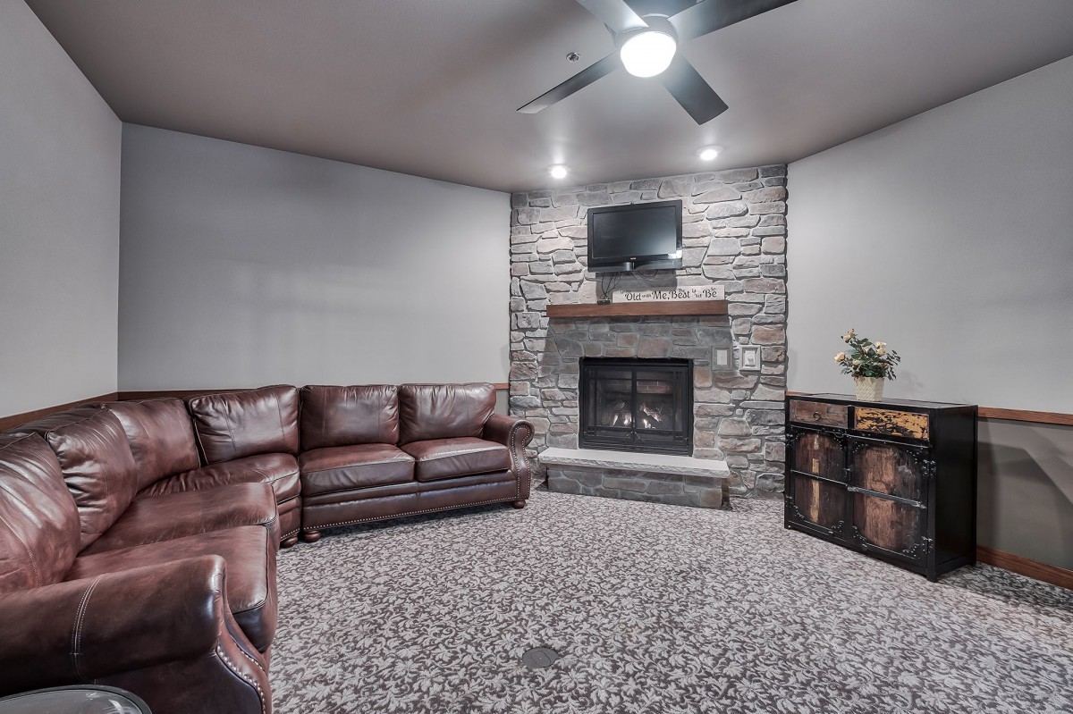 A cozy living room featuring a leather sofa, stone fireplace, and a television mounted above.