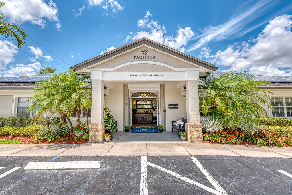 A building entrance with tropical landscaping and a parking area.