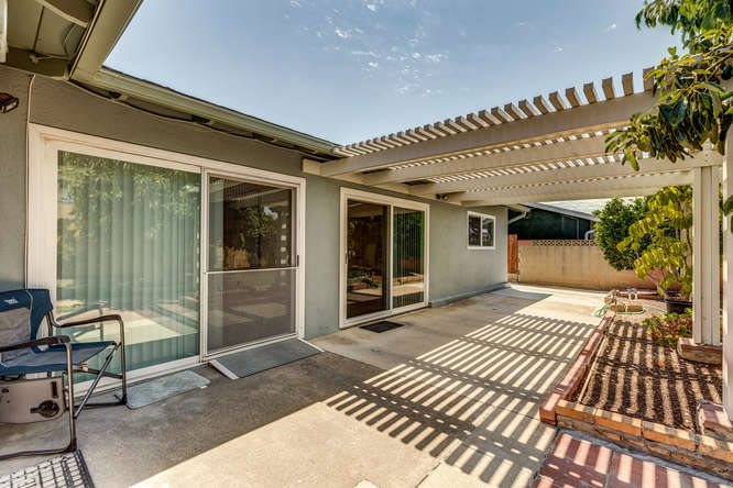 A residential outdoor patio area featuring a pergola and sliding glass doors.