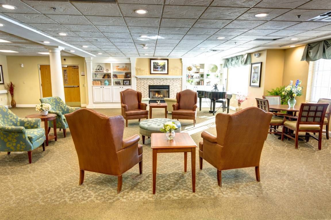 A cozy lobby with armchairs arranged around a central table, featuring a fireplace and piano in the background.