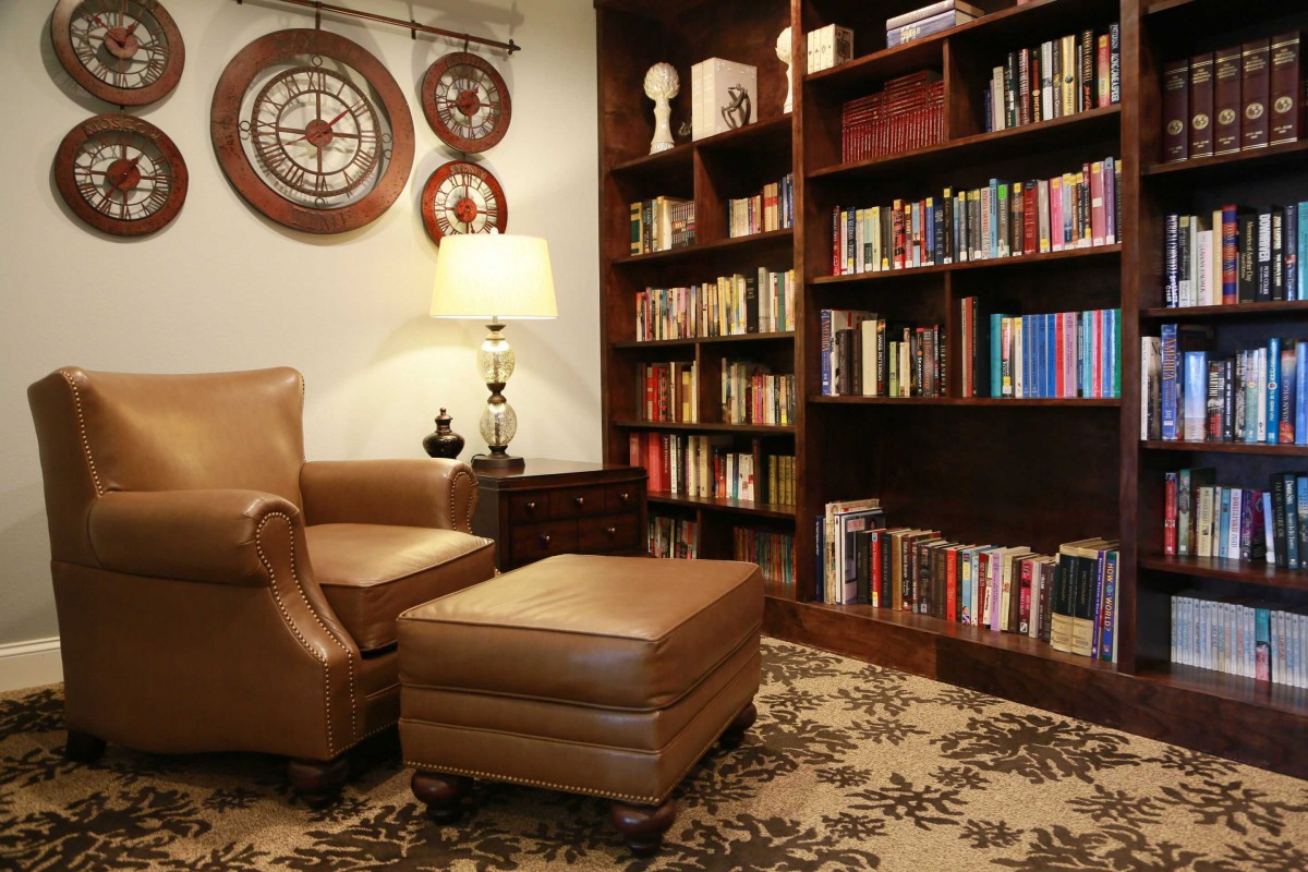 A cozy reading nook with a leather armchair, ottoman, and a wall of bookshelves.