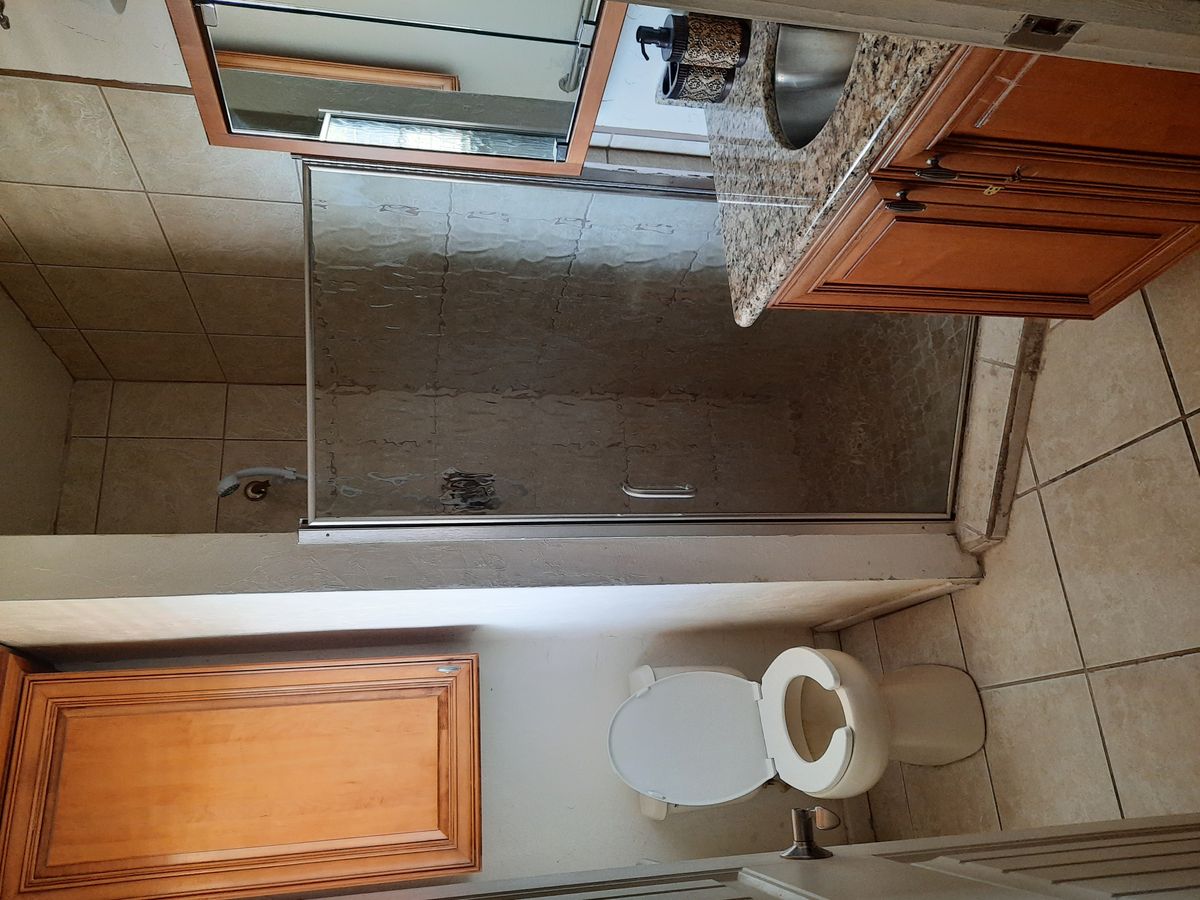 A clean bathroom featuring a toilet, sink, mirror, shower, and wooden cabinetry.