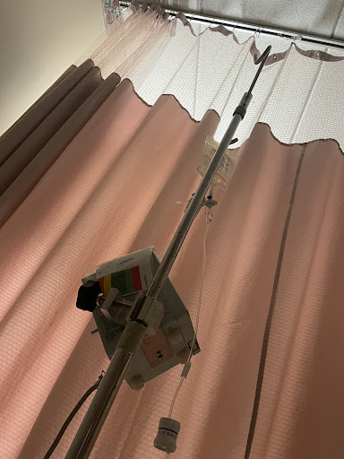 An IV pole with attached medical equipment stands beside a curtain in a hospital room.