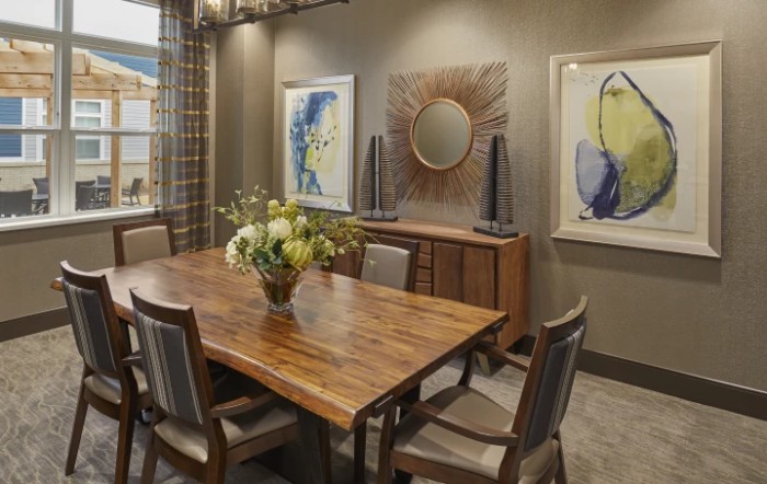 A modern dining room with a wooden table, surrounded by chairs, adorned with decorative artwork and a mirror on the walls.