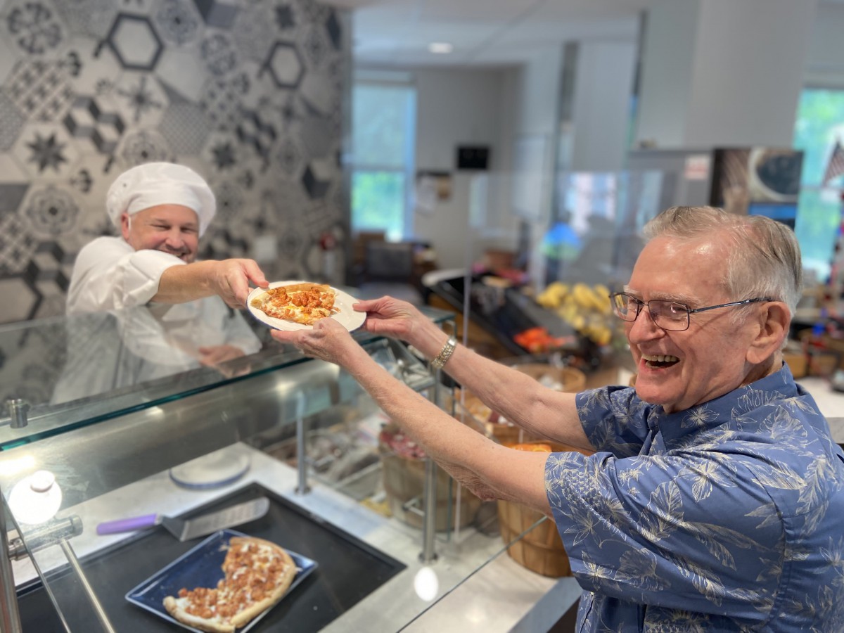 A happy customer receives a slice of pizza from a friendly chef behind the counter.