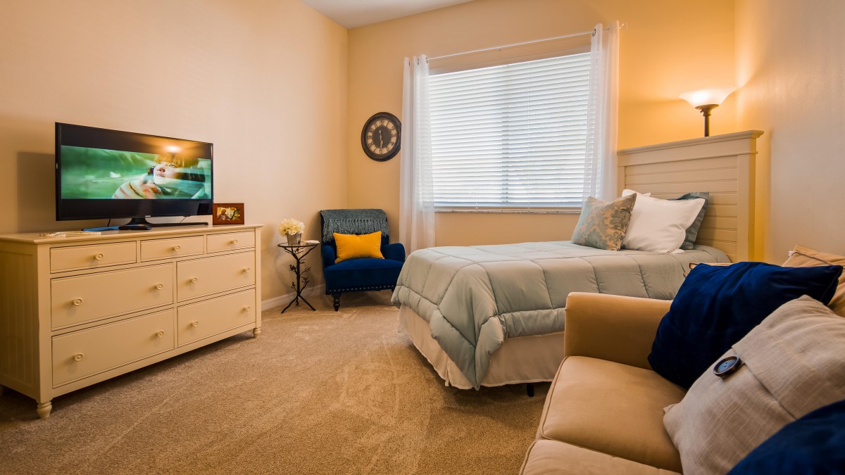 A cozy and well-decorated bedroom featuring a bed, armchair, dresser, and soft lighting.