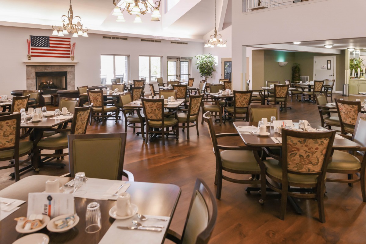 A spacious dining area with neatly arranged tables and chairs, featuring elegant chandeliers and a warm wooden floor.