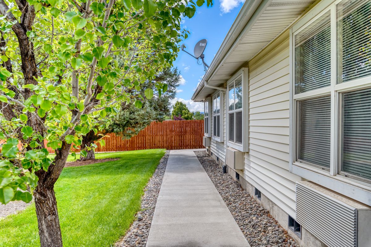 A walkway alongside a house with a well-maintained lawn and wooden fence.