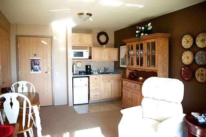 A cozy kitchen and living area with wooden cabinets, a microwave, and a compact refrigerator.