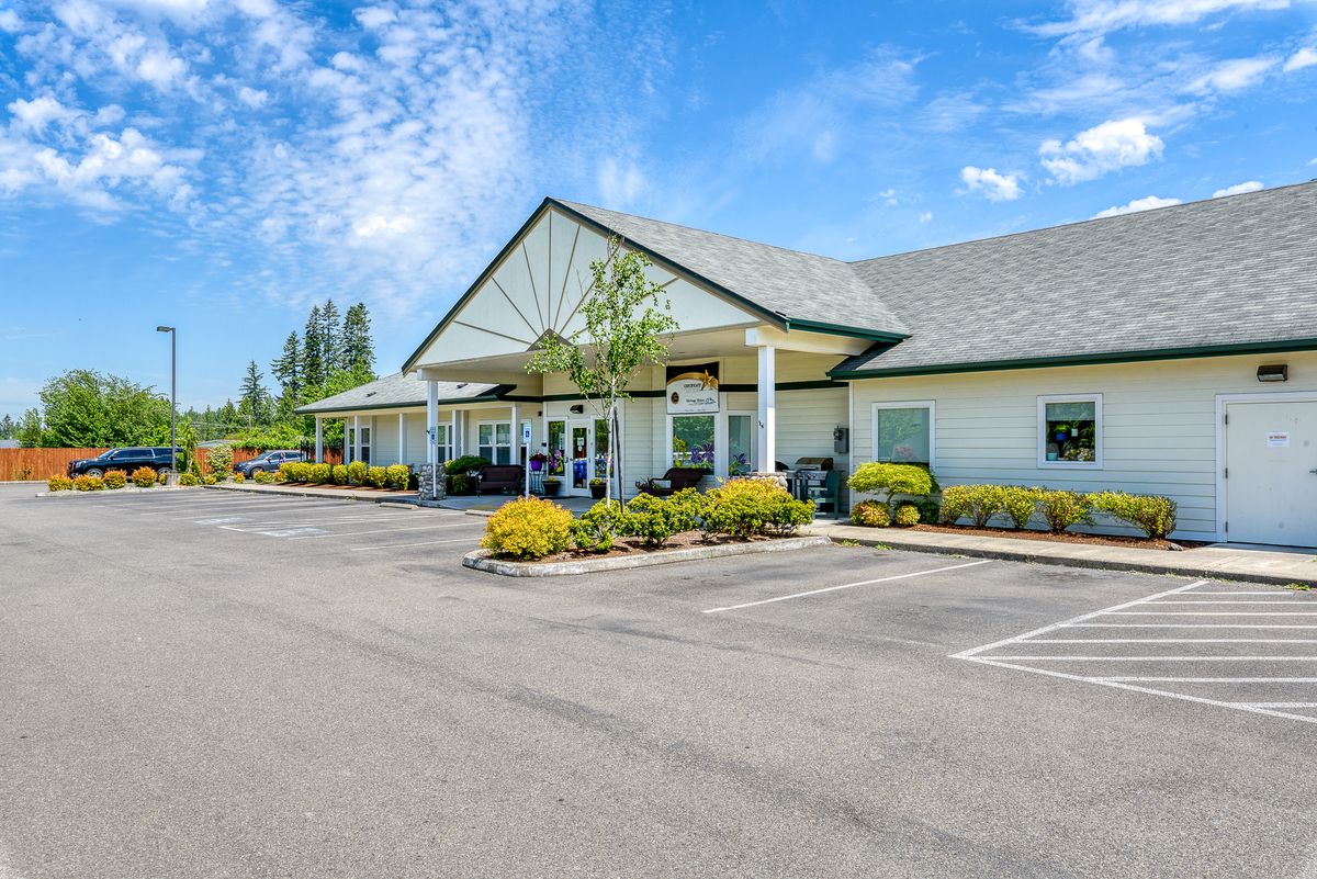 A single-story building with a parking lot and landscaping under a blue sky.