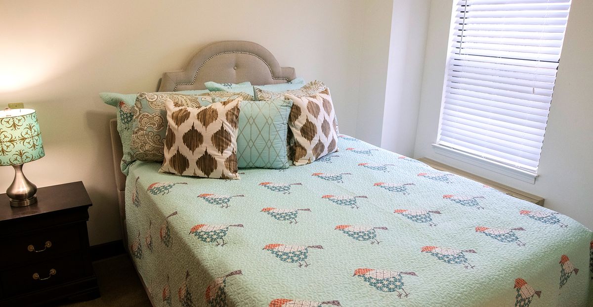 A cozy bedroom with a bed featuring chicken-patterned bedding and decorative pillows.