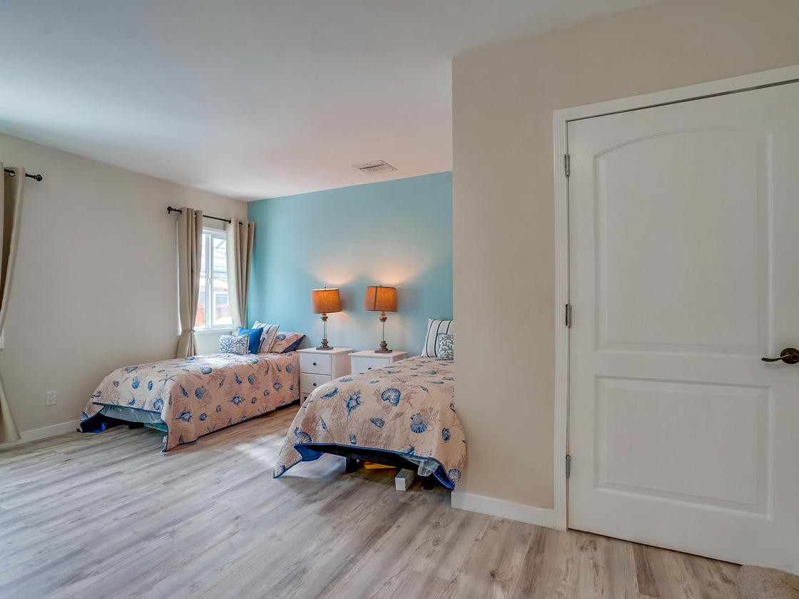 A cozy bedroom featuring twin beds with patterned bedding, a blue accent wall, and light wood flooring.