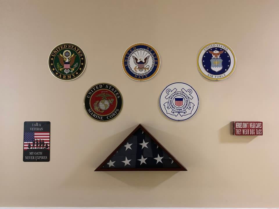 A wall displaying emblems of various U.S. military branches with a folded American flag below.