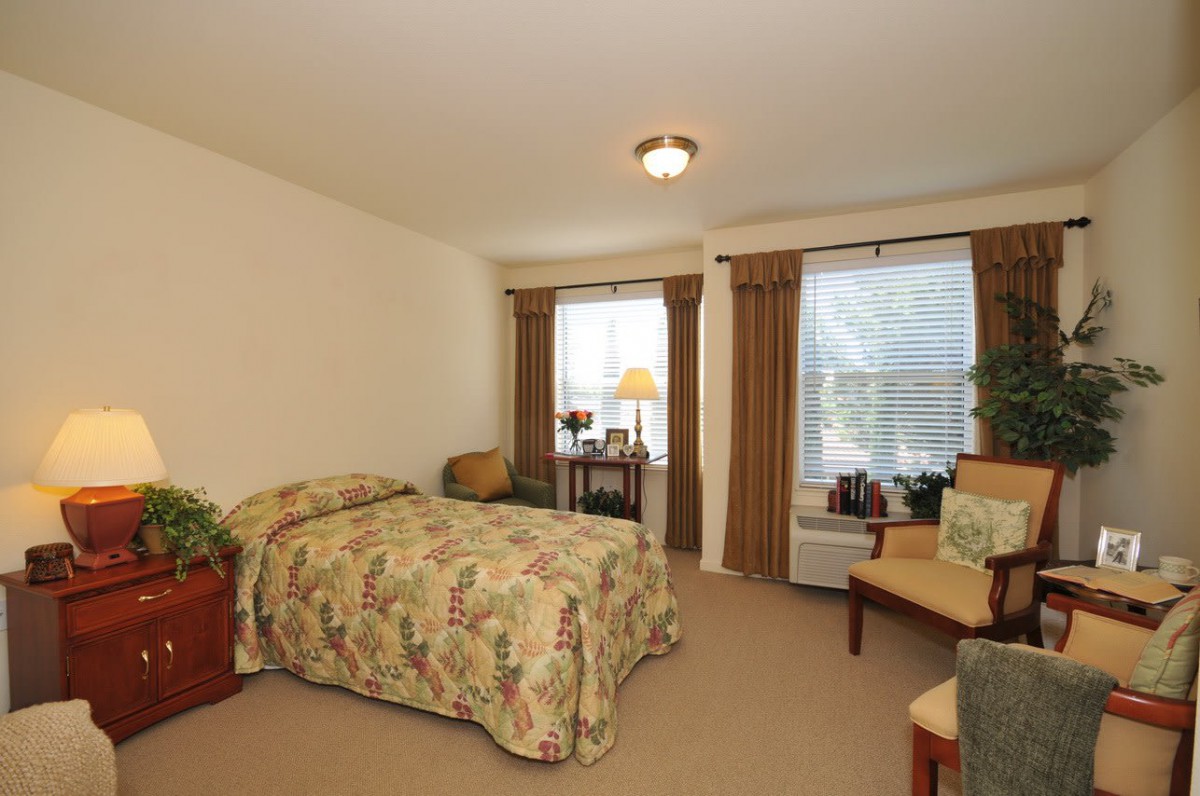 A cozy bedroom with a bed, two windows, and a small desk.