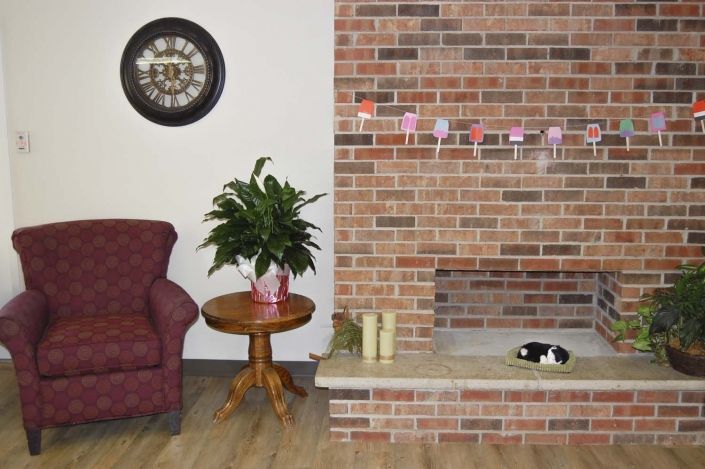 A cozy living room with a brick fireplace, an armchair, a side table with a plant, and decorative items.