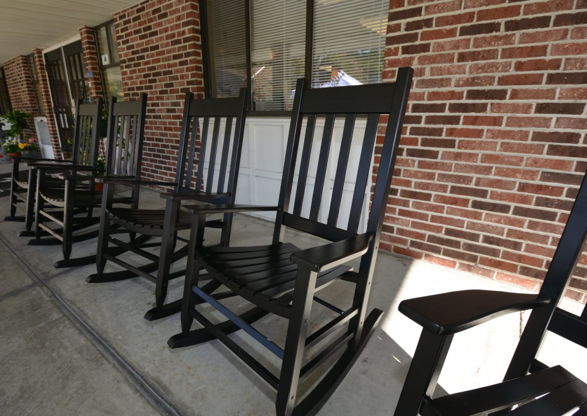A row of black rocking chairs on a porch with a brick wall backdrop.